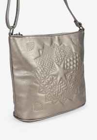 Bolso de hombro plateado metálico hecho de cuero texturizado, con un audaz diseño geométrico en relieve y correa ajustable. Cierre de cremallera en la parte superior.