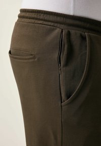 Donkergroene joggingbroek heeft een taps toelopend ontwerp, een elastische tailleband en een klein ritsvak aan de zijkant voor veilige opslag.