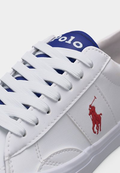 Λευκό αθλητικό παπούτσι με μπλε γλώσσα, λευκά κορδόνια και κόκκινο κεντημένο λογότυπο παίκτη πόλο στην πλευρική επιφάνεια.