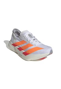 Zapatilla deportiva blanca con acentos en naranja y rosa. Parte superior de malla, punta redondeada, suela texturizada y diseño de tres franjas en el lateral.