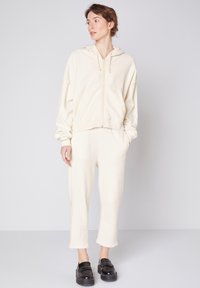Haut à zip en polaire et joggers assortis en crème. Caractéristiques : poignets côtelés, poches et coupe décontractée. Texture lisse avec un tissu doux et confortable.
