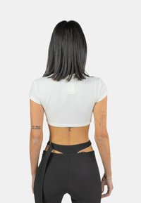 Top corto bianco a maniche corte con design aderente, abbinato a pantaloni neri a vita alta con dettagli a taglio e una cintura.