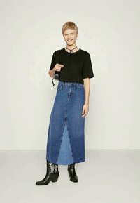 Haut noir à manches courtes, jupe maxi en denim bleu taille haute avec une fente à l'avant, associé à des bottes noires à talons et des chaussettes de cheville à motifs.