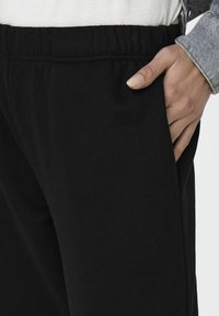 Pantaloni de trening negri, cu talie elastică, buzunar lateral și un material din bumbac confortabil. Textura pare netedă și moale.