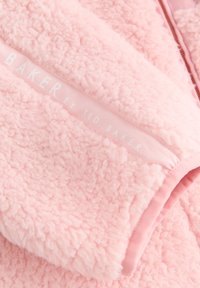 Tessuto in pile rosa morbido con cerniera e marchio bianco Ted Baker su una striscia diagonale di tessuto.