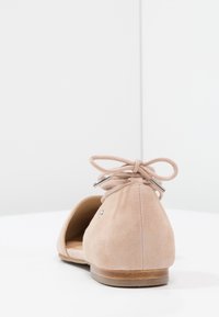 Ballerine in suede rosa chiaro con punta rotonda, lati aperti e chiusura con fiocco sul retro. Presentano un tacco in legno liscio e un sottile accento metallico.