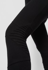 Leggings noires avec des panneaux texturés et des détails de couture, dotés d'un design ajusté et d'un tissu lisse et extensible pour le confort et la flexibilité.