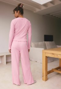 Ružový dlhý rukáv top s vlnitým lemom skombinovaný s ružovými voľnými nohavicami. Textúrovaná látka, voľný strih, nosené s mäkkými šedými papučami.