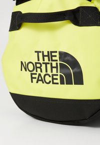 Žltý vodeodolný batoh s čiernou základňou, ktorý na sebe má čierny potlačený logotyp "THE NORTH FACE" a odolné hardvérové prvky na popruhoch.