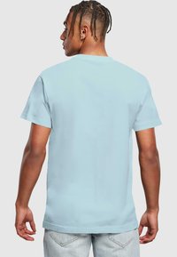 Lichtblauw T-shirt met korte mouwen, gemaakt van katoen, met een ronde hals, gladde textuur, zichtbare stiksels, gedragen met lichtgekleurde jeans.