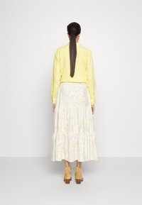 Keltainen pellavapaita yhdistettynä kukkakuosiseksi, kerrokselliseksi maksihameeksi, jossa on keltaisia ja harmaita kuvioita. Vaaleanruskeat nilkkurit täydentävät asua.