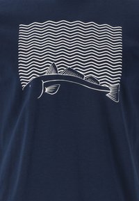 Mörkblå bomulls t-shirt med en vit grafik av en fisk över böljande linjer, med en enkel, ren design och slät textur.
