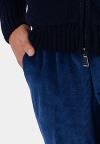 Granatowy sweter z dzianiny z prążkowanym dołem i teksturowanym materiałem, zestawiony z niebieskimi spodniami z korduroyu w pionowe paski i akcentem w postaci zamka.