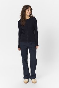 Námořnický cardigan s kulatým výstřihem a zapínáním na knoflíky, v kombinaci s tmavě námořnickými kalhotami a světlými botami. Hladká textura a přiléhavý střih.