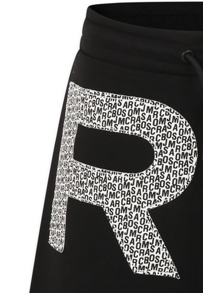 Pantalons de survêtement noirs avec un grand graphique blanc en forme de "R" composé de motifs textuels répétés. Comprend une taille élastique et des détails de cordon de serrage.