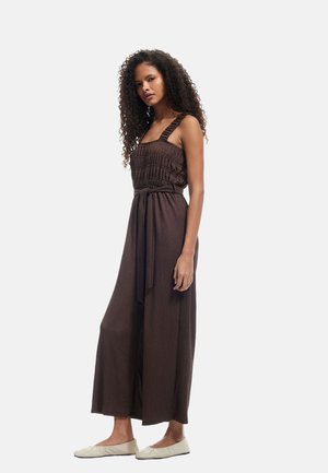 Brown jumpsuit with smocked bodice and wide-leg pants, featuring thick straps and a tie belt. Smooth texture and relaxed fit.