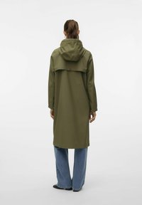Dolga olivno zelena dežna plašča s kapuco, z gumbastim preklopom čez ramena in stranskimi žepi. Nosena čez ohlapne modre kavbojke.