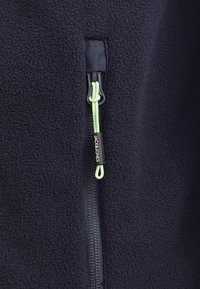 Chaqueta de forro polar en color navy con un suave zipper y una lengüeta verde, etiqueta de logo y tejido texturizado para calidez y comodidad.