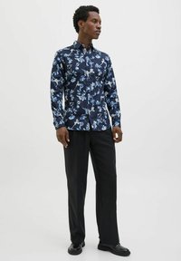 Camicia floreale blu navy con motivi blu e bianchi, design con bottoni, maniche lunghe, abbinata a pantaloni e scarpe neri.
