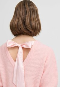 Roze gebreide trui met een V-hals en een open rug, met een satijnen strik bij de halslijn. De stof lijkt zacht en gestructureerd.