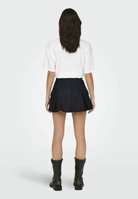 Svart denim mini kjol med veck och fransad nederkant, försedd med två sidofickor. Kombineras med en lös vit T-shirt och svarta stövlar.