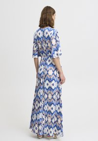 Robe longue et fluide en bleu, blanc et pêche avec un motif en zigzag. Fabriquée dans un tissu léger, elle présente une taille à nouer et des manches larges.