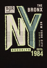 Maglietta nera con testo stratificato audace in vari colori: "NY", "The Bronx" e "New York City". Include accenti e motivi a righe.