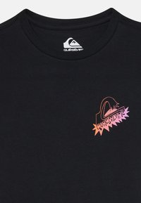T-shirt preta de algodão com gola redonda, apresentando um logótipo multicolorido da Quiksilver no lado esquerdo do peito, misturando tons de rosa e laranja.