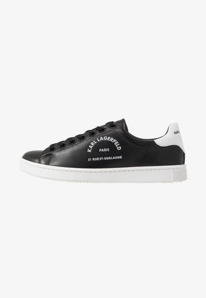 Zapatilla negra de corte bajo con suela blanca y tira en el talón, cordones negros, texto "Karl Lagerfeld Paris 21 Rue St-Guillaume" en el lateral.