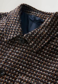 Woven outerwear jacket featuring a textured navy, brown, and white pattern, large collar, and a black button near the neckline.