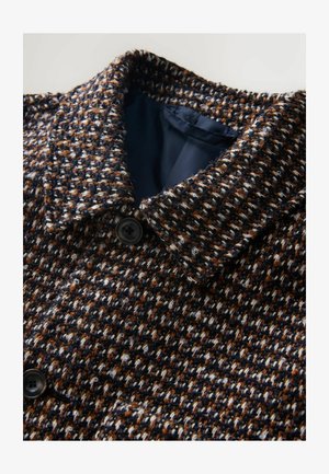 Tkany płaszcz z wzorem w odcieniach granatu, brązu i bieli, z dużym kołnierzem i czarnym guzikiem blisko dekoltu.