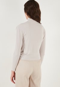 Lichtgrijs lange mouwen coltrui met zachte, gladde stof. De zoom zit op de taille, met aansluitende mouwen en een minimalistisch ontwerp.