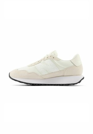 Helle beige Laufschuhe mit einem Obermaterial aus Wildleder und Mesh, das ein strukturiertes weißes Logo, eine schwarze Außensohle und ein einfaches Schnürdesign aufweist.