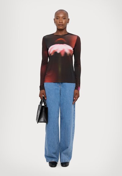Top nero a maniche lunghe con fantasia floreale, abbinato a jeans a gamba larga di un blu chiaro. La modella tiene una piccola borsa nera. Tessuto morbido.