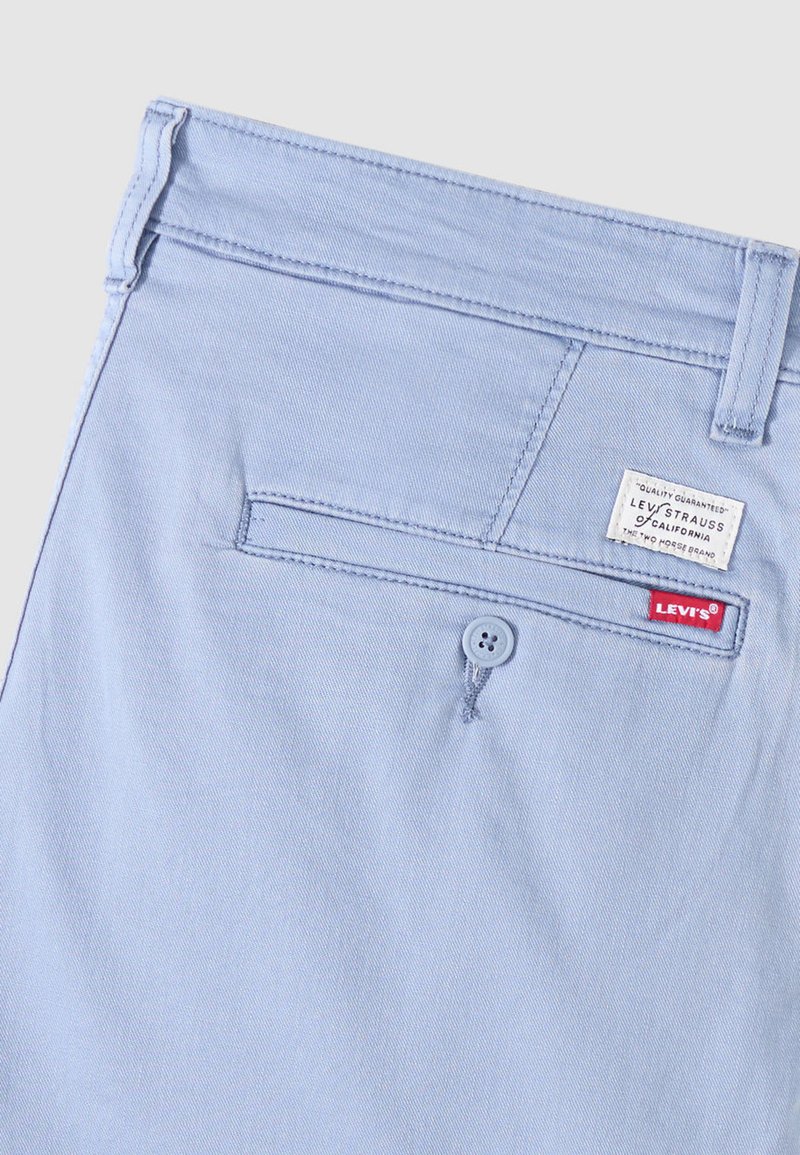 Poche arrière d'un pantalon Levi's bleu clair avec fermeture à bouton, passants de ceinture cousus et étiquettes de la marque Levi's visibles en rouge et blanc.