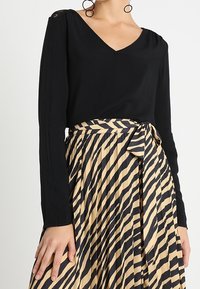 Haut noir à manches longues avec col en V et détail froncé aux épaules, associé à une jupe plissée ornée de rayures zèbre noires et beiges et une taille nouée.