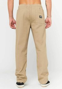 Lysbrune, løstsiddende bukser med elastisk talje, en baglomme med et logopatch og et glat, tekstureret stof.