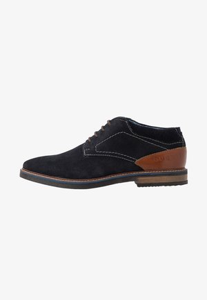 Chaussure de ville pour homme en daim noir à lacets, avec un patch en cuir brun au talon, des surpiqûres contrastantes et une semelle en bois empilée.