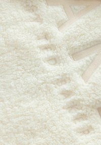 Coperta in pile color crema con una superficie morbida e texturizzata. Presenta testo in rilievo e un nastro liscio e a contrasto lungo il bordo.