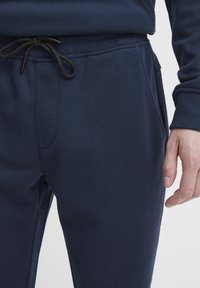 Marineblauwe joggingsbroek van textuurstof, met een elastische tailleband met koord en zijzakken.