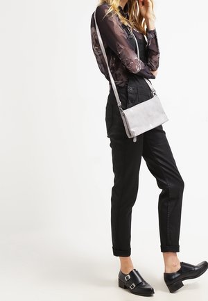 Grau Umhängetasche mit glatter Textur und dezenter Naht, ausgestattet mit einem langen Tragegurt, kombiniert mit einem transparenten gemusterten Oberteil und schwarzen Hosen.