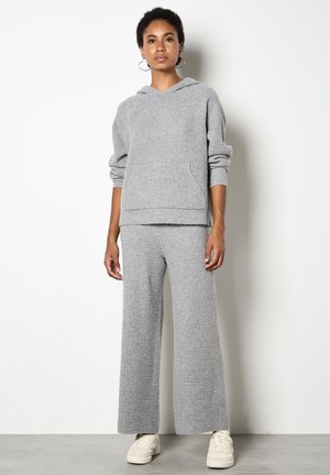 Szara dzianinowa bluza z kapturem z kieszenią oraz szerokimi spodniami w komplecie. Miękka tekstura, luźny krój i swobodny design. Białe sneakersy dopełniają stylizację.