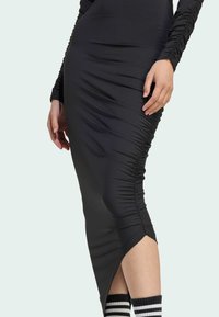 Svart klänning med lång ärm, figurnära passform, med samlad detalj på sidorna och en hög slits vid låret. Texturerat, elastiskt tyg.