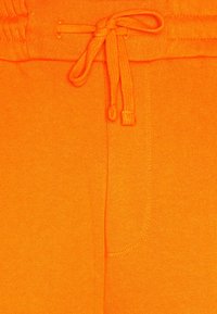 Nahaufnahme von leuchtend orangefarbenen Stoffshorts mit einem gebundenen Kordelzug und sichtbaren Nähten im Bereich des Bundes und der Taschen.