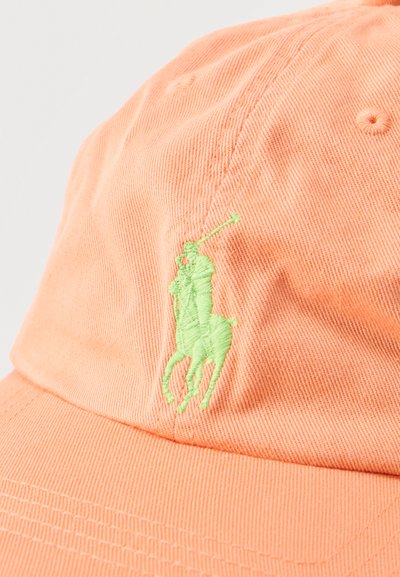 Κοντινό πλάνο ροδακινί καπέλου με πράσινο κεντημένο λογότυπο ενός παίκτη πόλο έφιππου που κρατάει ένα ρόπαλο.