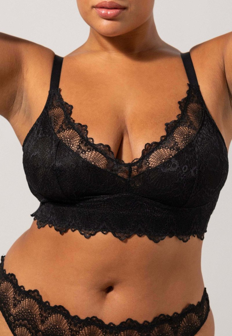 Mustavillainen pitsinen bralette, jossa on aaltoilevat reunat, säädettävät olkaimet ja V-mallinen kaula-aukko. Pehmeä pinta, jossa on monimutkaisia kukkakuoseja.