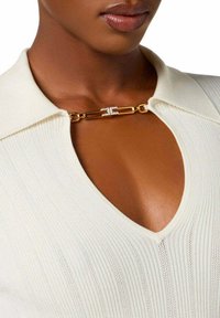Top color crema con un design a coste testurizzato, dotato di scollo a V e un accento in metallo dorato con piccoli strass.