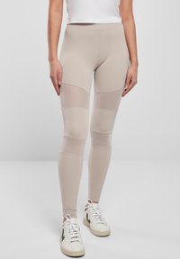 Bež legice s mrežastim panelima, glatke teksture i elastičnim pojasom. Uparene s bijelim tenisicama.