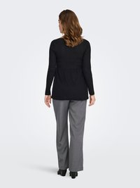 Haut noir à manches longues avec un design péplum, associé à un pantalon gris à jambes larges. La tenue présente des textures lisses et une coupe ajustée.