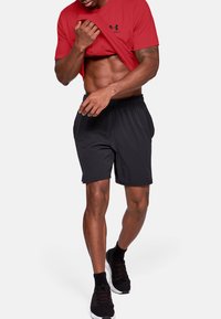 T-shirt de sport rouge à manches courtes avec un logo noir, associé à un short noir à taille élastique et des baskets noires à semelles texturées.